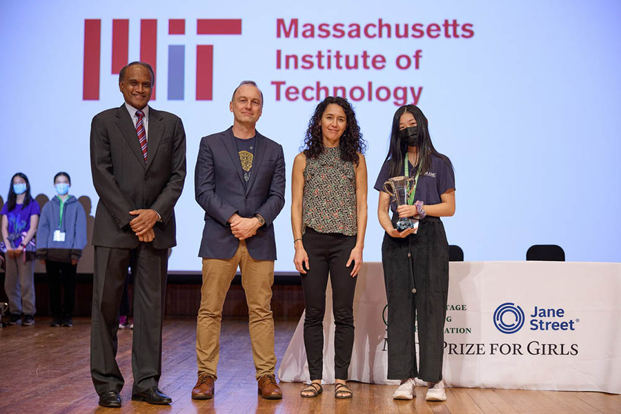 Four people on a stage, with winner Jessica Wan holding a trophy. 