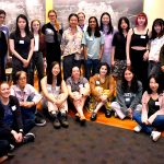 Group of female attendees standing in two rows, blackboard behind them.